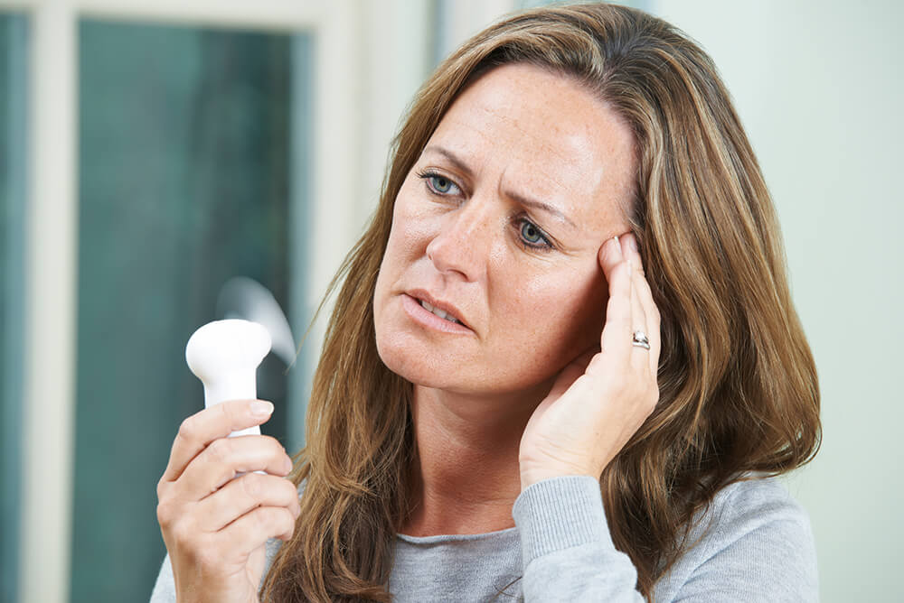 Photo of a hot, worried woman holding a fan